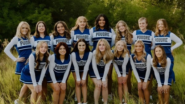 Un grupo de jóvenes estudiantes en uniforme de animadoras posan juntas en un campo en Poudre School District.