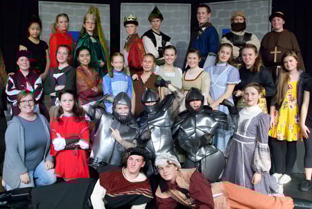 Un grupo de estudiantes de la Prairie Christian Academy posan juntos en varios disfraces frente a un fondo oscuro con elementos arquitectónicos.