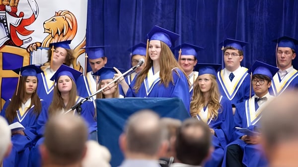 Graduadas y graduados de la Prairie Christian Academy están en togas azules en el escenario frente a una cortina azul.
