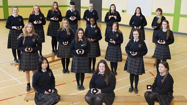 Un grupo de estudiantes del Presentation College Carlow está en el gimnasio con su uniforme escolar.