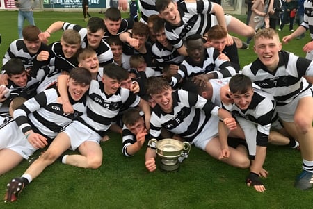 Los estudiantes del Presentation College Carlow celebran en un campo con un trofeo en la mano.