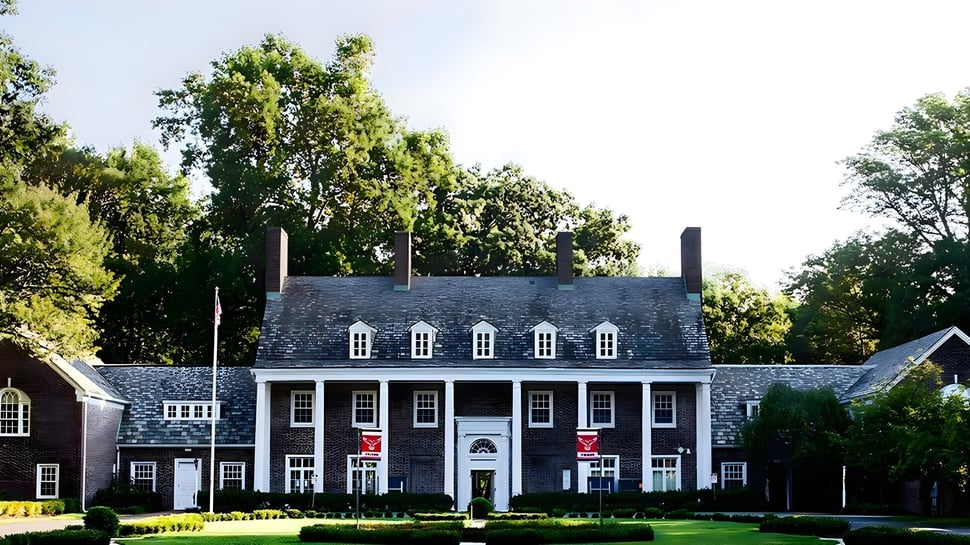 Una mansión de estilo colonial se encuentra en el terreno de la Princeton International School of Mathematics & Science rodeada de árboles y césped bien cuidado.