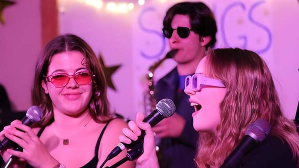 Tres personas de la Proctor Academy actúan con micrófonos en un escenario colorido.