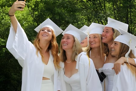 Un grupo de graduadas de la Proctor Academy está juntas en togas de graduación blancas al aire libre.