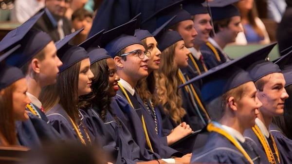 Un grupo de graduados y graduadas de la Providence Christian Academy se encuentra en una ceremonia solemne con vestimenta académica.