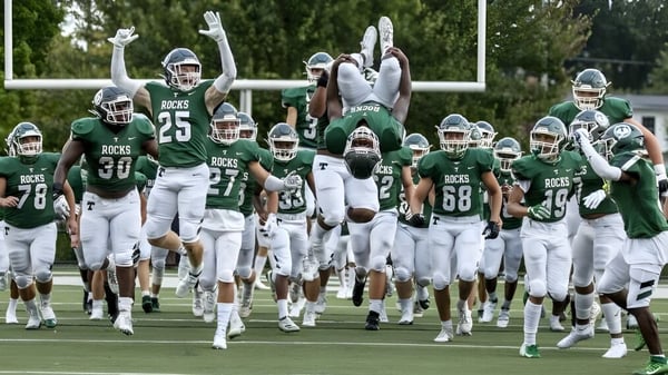 Un grupo de jugadores de fútbol en uniformes verdes y blancos corre en el campo del Provo City School District.