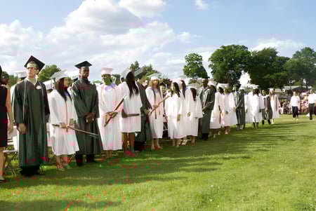 Un grupo de graduadas y graduados del Provo City School District está de pie en un campo con árboles y un cielo nublado de fondo.