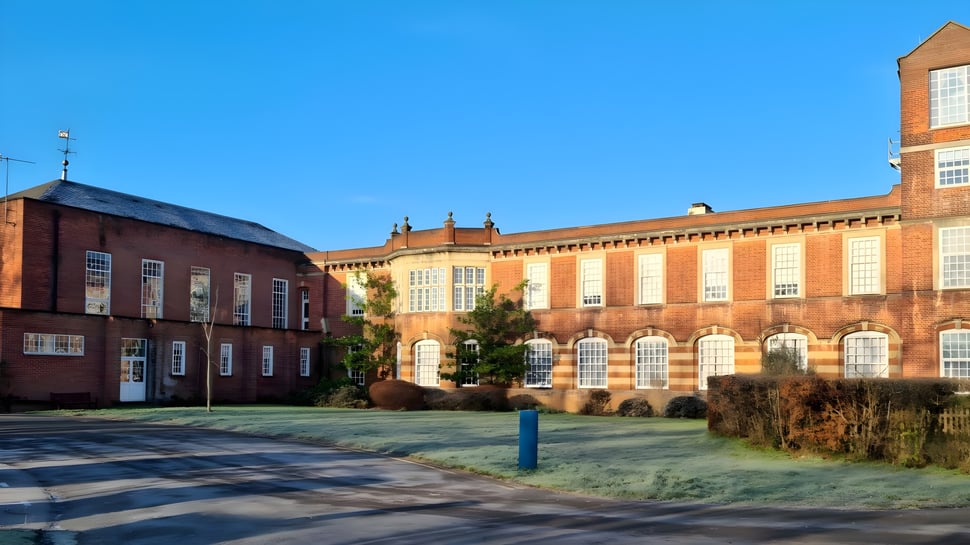 El edificio de ladrillo de The Purcell School for Young Musicians está rodeado de un área verde con un paso peatonal.