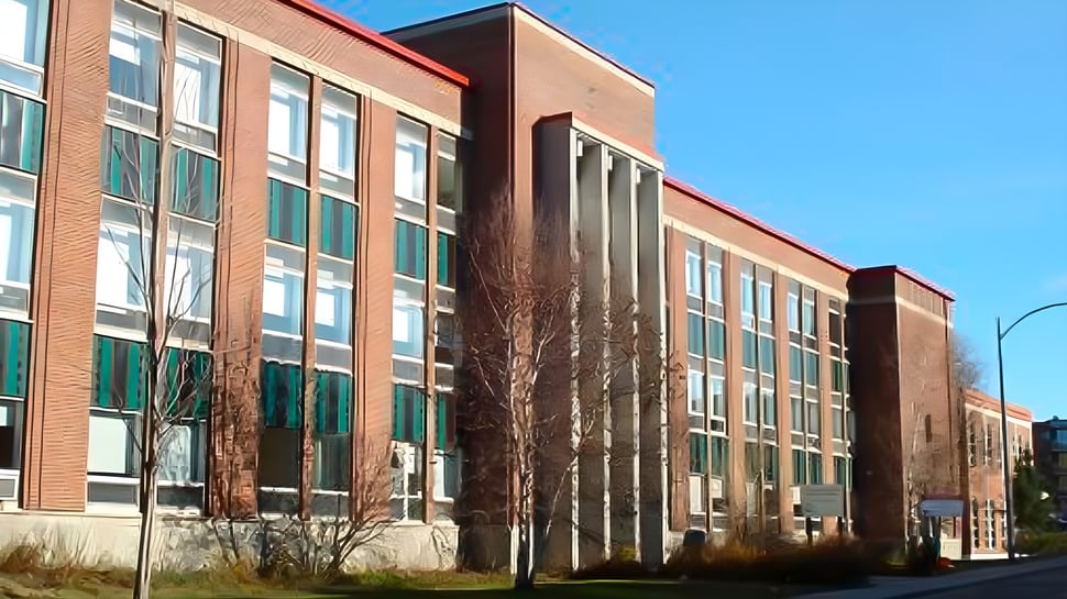 El edificio de ladrillo de varios pisos de la Québec High School con grandes ventanas y una entrada destacada frente a un cielo azul claro.