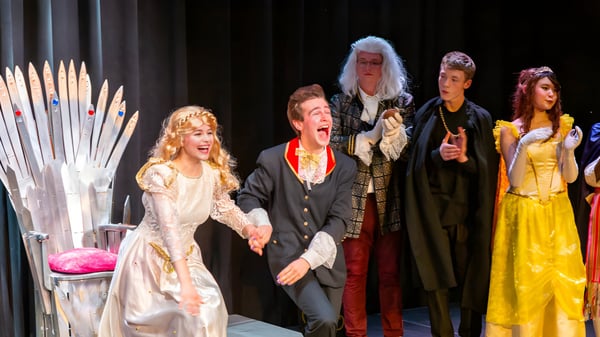 Estudiantes de la Québec High School están en trajes coloridos sobre un escenario frente a un telón.