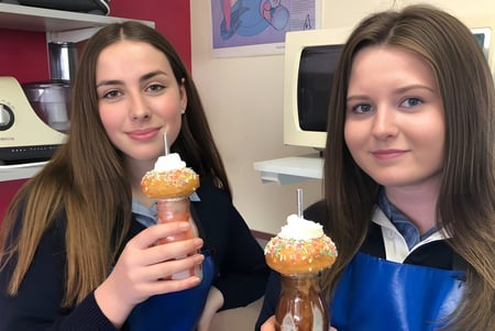 Dos estudiantes de la Queechy High School sostienen helados en una cocina con decoración colorida.