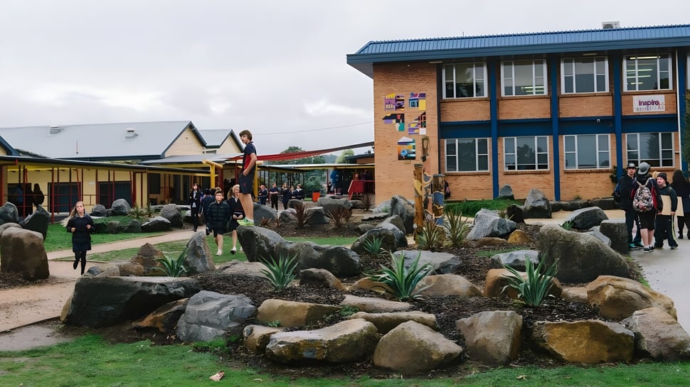 El patio de la Queechy High School muestra varios edificios y estudiantes que se mueven por el terreno.