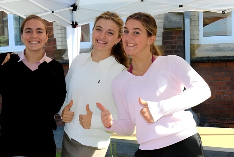 Tres estudiantes sonrientes están frente a un edificio en el campus de la Queen Anne’s School.