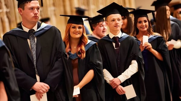 Un grupo de graduadas y graduados en vestimenta académica está juntos en la ceremonia de graduación de Queen Ethelburga’s Collegiate.