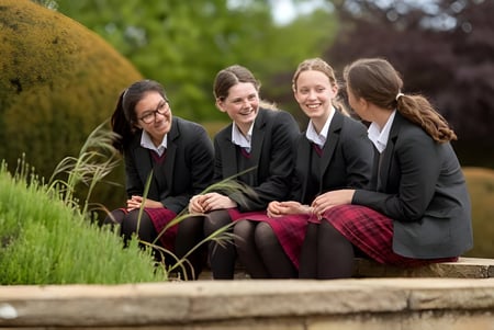 Cuatro alumnas de la Queen Margaret's School for Girls están sentadas juntas en un banco de madera en el campo.
