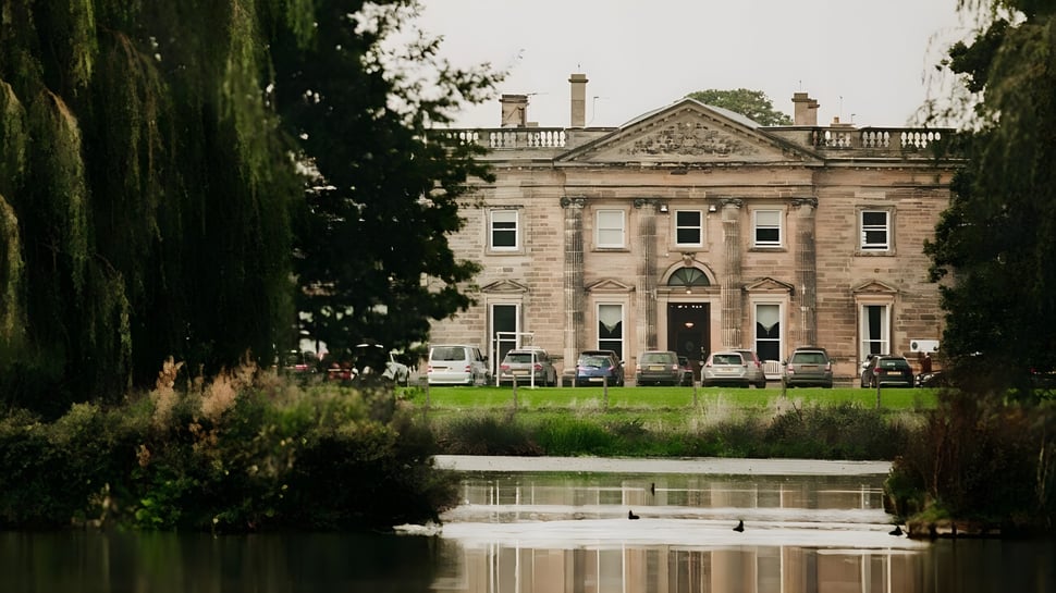 La histórica mansión en el terreno de la Queen Mary's School se refleja en el tranquilo estanque frente al edificio.
