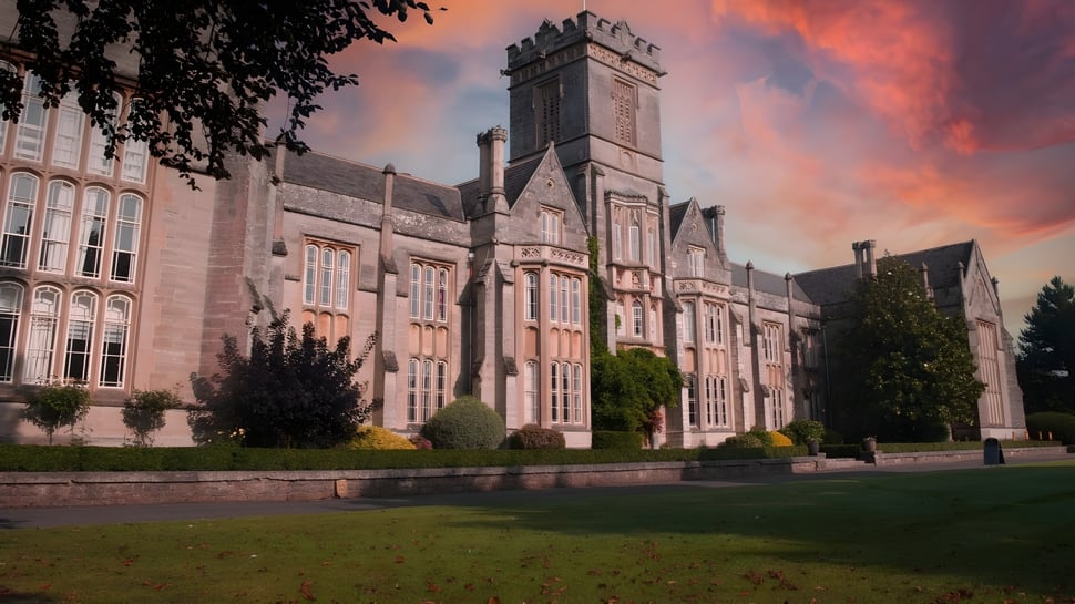 El edificio histórico del Queen’s College está rodeado de un paisaje verde bajo un cielo dramáticamente rojo.