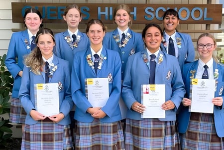 Estudiantes de la Queens High School reciben sus certificados frente al edificio escolar.