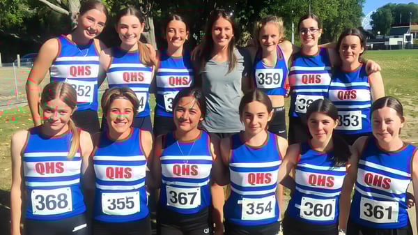 Un grupo de estudiantes de la Queens High School está en uniformes deportivos azules y blancos en un campo deportivo.