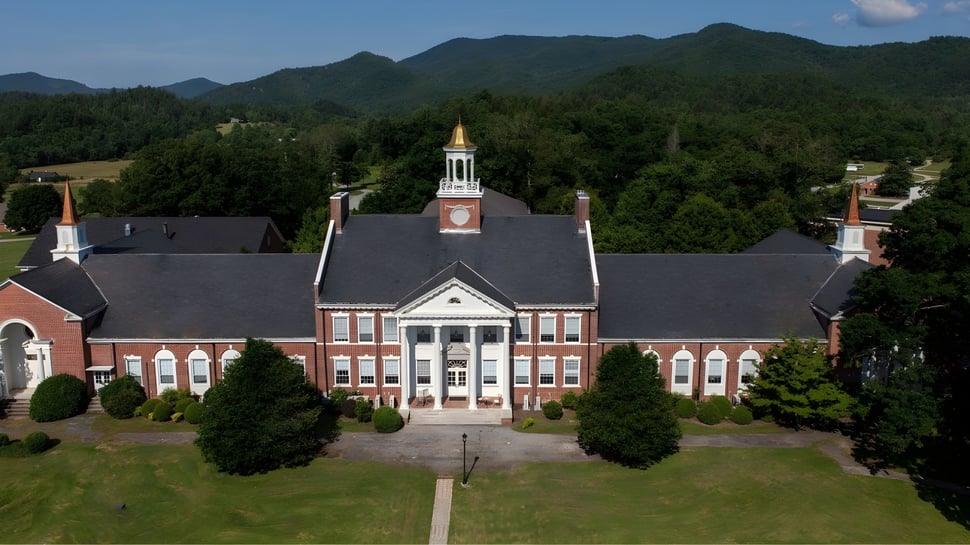 El edificio de ladrillo con torre del reloj de la Rabun Gap-Nacoochee School está rodeado de áreas verdes y montañas.