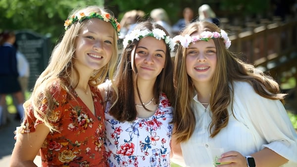 Tres estudiantes con coronas de flores sonríen al aire libre en el campus de la Rabun Gap-Nacoochee School.