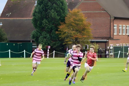 Estudiantes del Radley College juegan en un campo de césped frente a un edificio de ladrillo en un deporte de equipo.