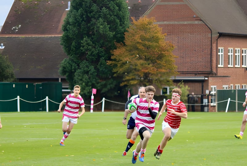 Estudiantes del Radley College juegan en un campo de césped frente a un edificio de ladrillo en un deporte de equipo.
