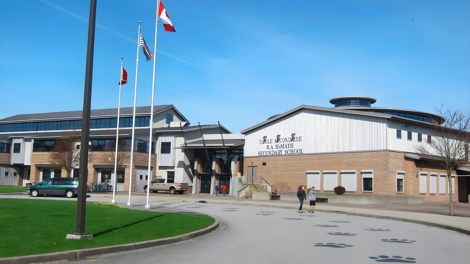El moderno edificio de varios pisos de la École Secondaire R.A. McMath Secondary School con banderas y un camino en primer plano.