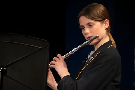 Una joven estudiante del Ratcliffe College toca una flauta en el escenario frente a un fondo negro.