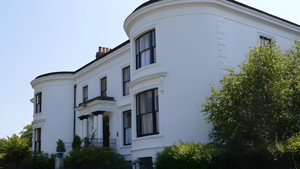 El edificio blanco con detalles arquitectónicos curvos en el campus de la Rathdown School está rodeado de un exuberante jardín.