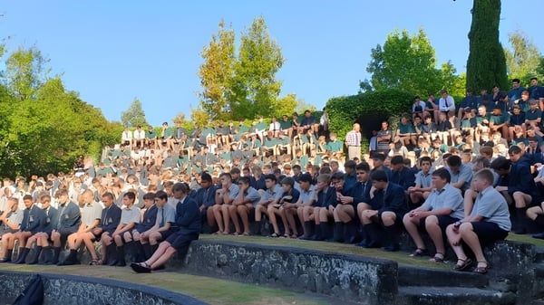 Un grupo de estudiantes se sienta en un muro de piedra frente a árboles en el terreno de Rathkeale College.
