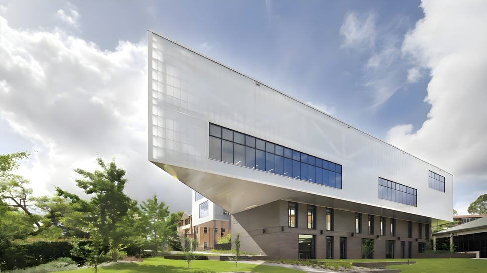 El moderno edificio de la Ravenswood School for Girls con grandes ventanas y rodeado de un paisaje verde se ve ante un cielo nublado.