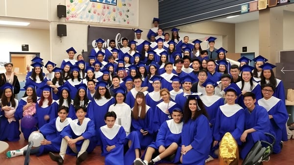 Un gran grupo de graduados de la R.C. Palmer Secondary School posa con togas azules en un aula.