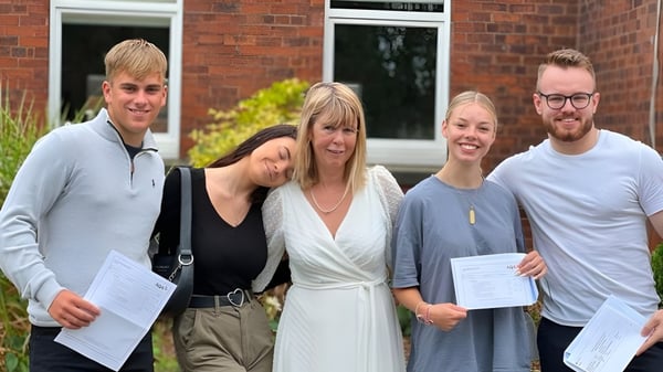 Cuatro estudiantes de la Read School están frente a un edificio de ladrillo sosteniendo certificados.