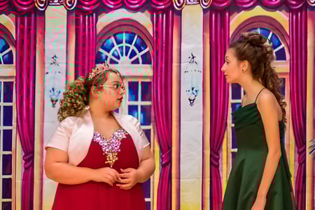 Dos estudiantes de la Red Creek High School están frente a un fondo colorido con arcos y cortinas.