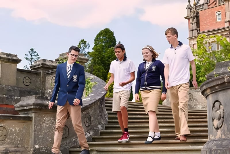 Estudiantes de Reddam House Berkshire suben juntos una escalera de piedra frente a un edificio histórico.