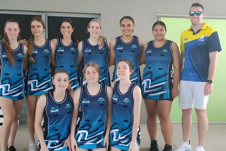 Un grupo de jóvenes atletas posan con uniformes azules y blancos frente a un edificio en el campus de Redlynch State College.