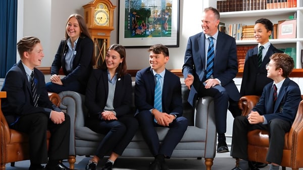 Un grupo de estudiantes se encuentra en una sala con un gran reloj y estanterías en el campus de la Reed’s School.