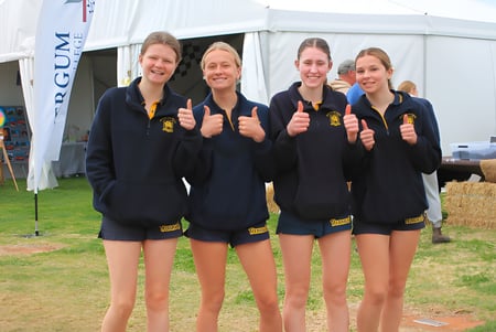 Cuatro alumnas de la Renmark High School están juntas frente a un techo de carpa blanca y muestran el pulgar hacia arriba al aire libre.
