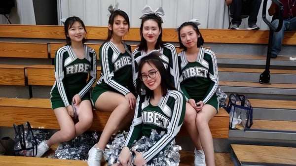 Un grupo de estudiantes de Ribet Academy posan juntas en uniformes deportivos frente a un gimnasio.