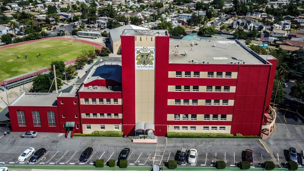 Un gran edificio rojo de Ribet Academy se encuentra frente a un amplio paisaje urbano.