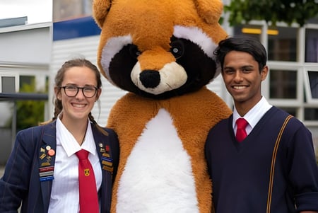 Dos personas con ropa formal están de pie frente a una gran escultura de un animal en el campus de la Riccarton High School.