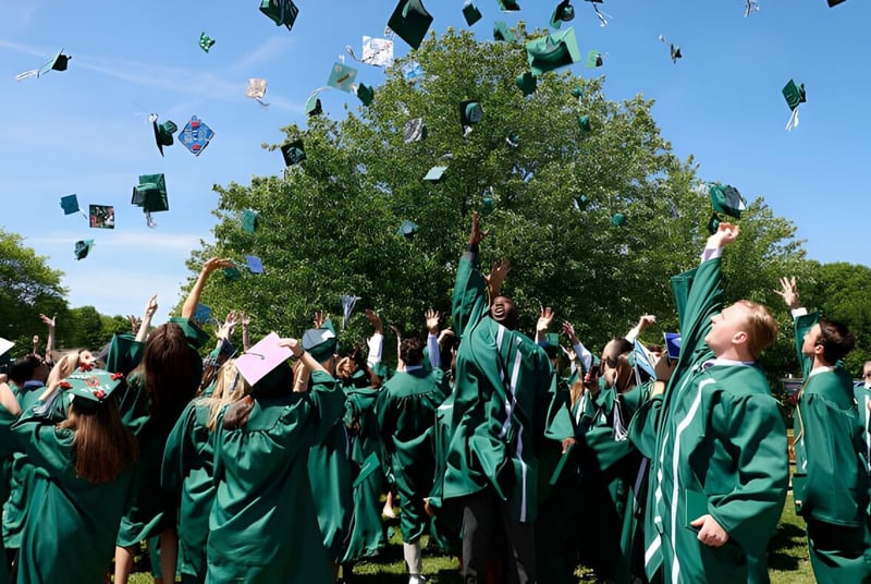 Los graduados de la Rice Memorial High School están debajo de un árbol y lanzan sus sombreros al aire.