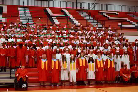 Un gran grupo de estudiantes de la Richmond High School se reúne en el gimnasio para la ceremonia de graduación.