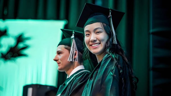 Dos graduados en togas de graduación verdes de la Rick Hansen Secondary School están frente a un fondo verde.