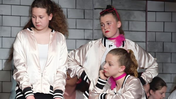 Tres alumnas de la Ridgetown District High School están frente a una pared de concreto gris.
