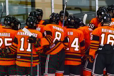 Un grupo de jugadores de hockey en camisetas naranjas está junto a un edificio en el campus del Ridley College.