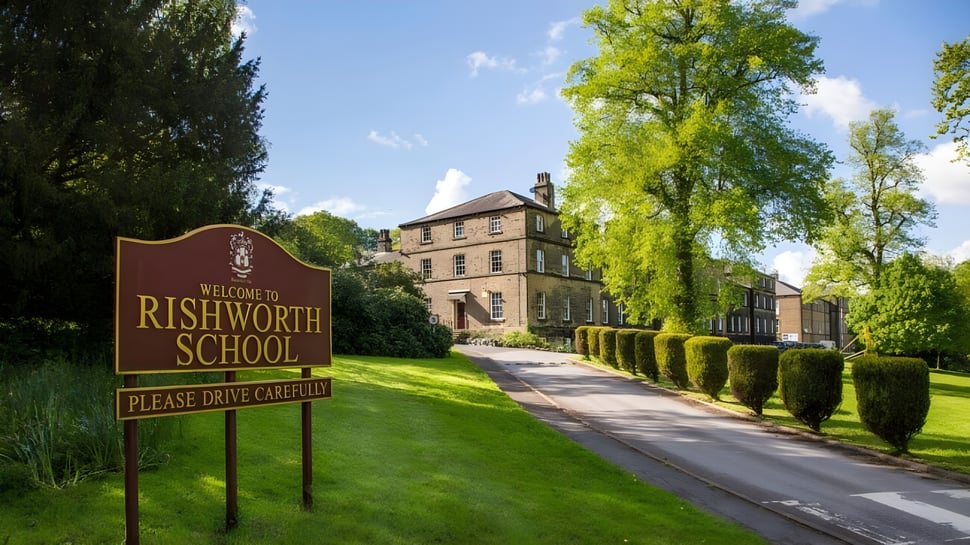 El cartel de bienvenida de la Rishworth School está frente a un edificio histórico y rodeado de mucho verde.
