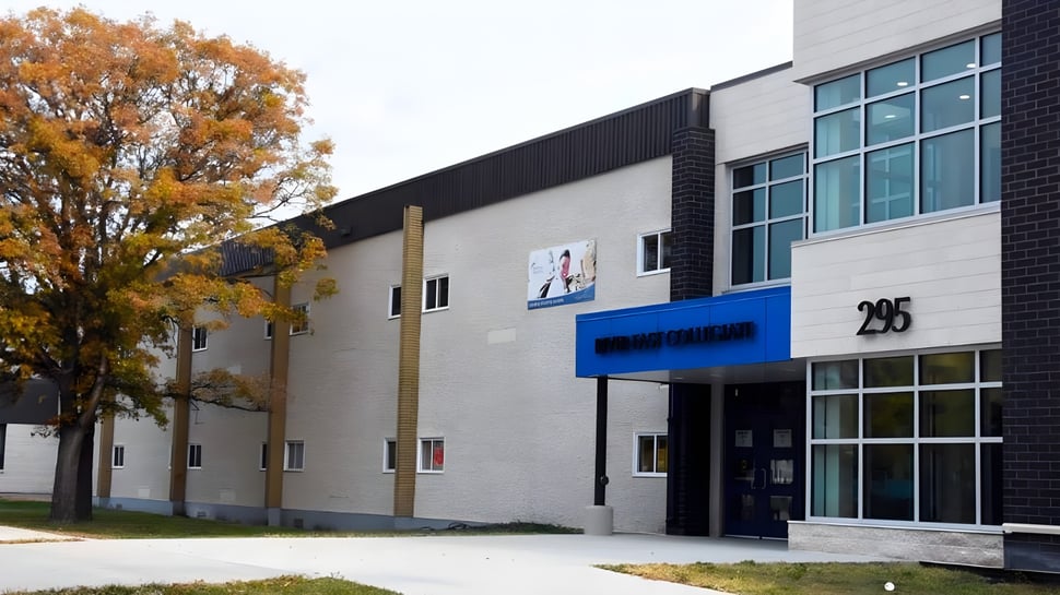 El moderno edificio de varios pisos del River East Collegiate está rodeado de árboles con hojas otoñales.