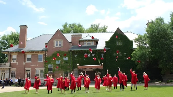 Un grupo de personas con túnicas rojas está de pie en un campo frente a un edificio de ladrillo en el campus del Rivermont Collegiate.